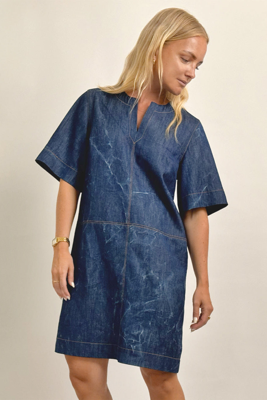 Woman wearing a blue denim dress against a beige background